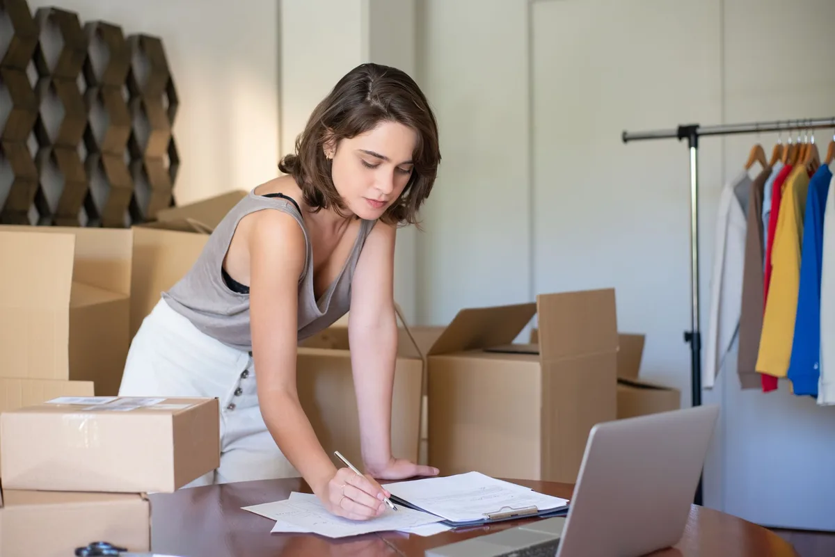 Ecommerce store owner working on a laptop surrounded by packaging boxes while managing her online store