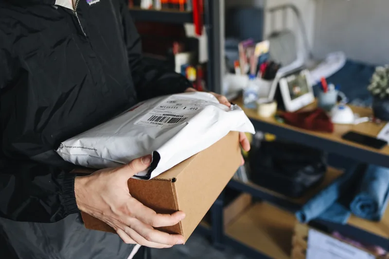 Close-up of hands holding cardboard and plastic packages, representing an order a customer is waiting to receive confirmation and tracking details for