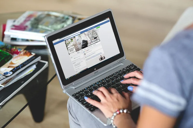 A woman typing on a laptop with social media on the screen