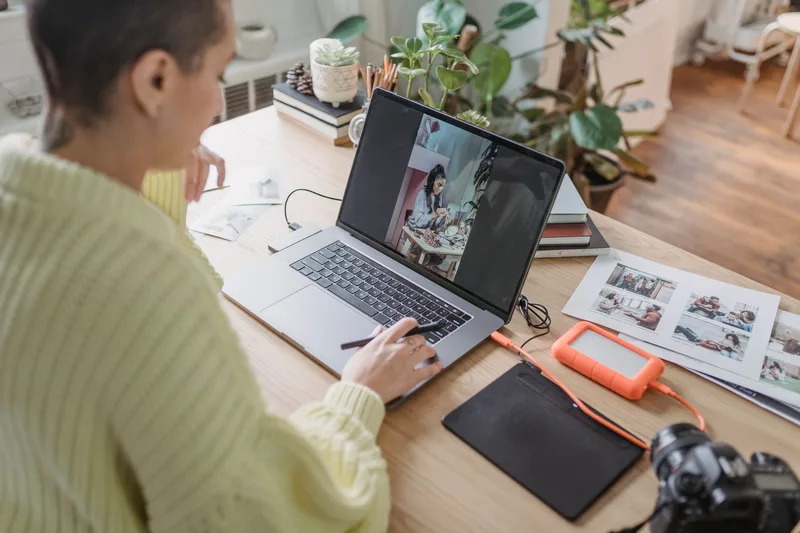 Person editing product photos on a laptop with a camera and printed photos nearby